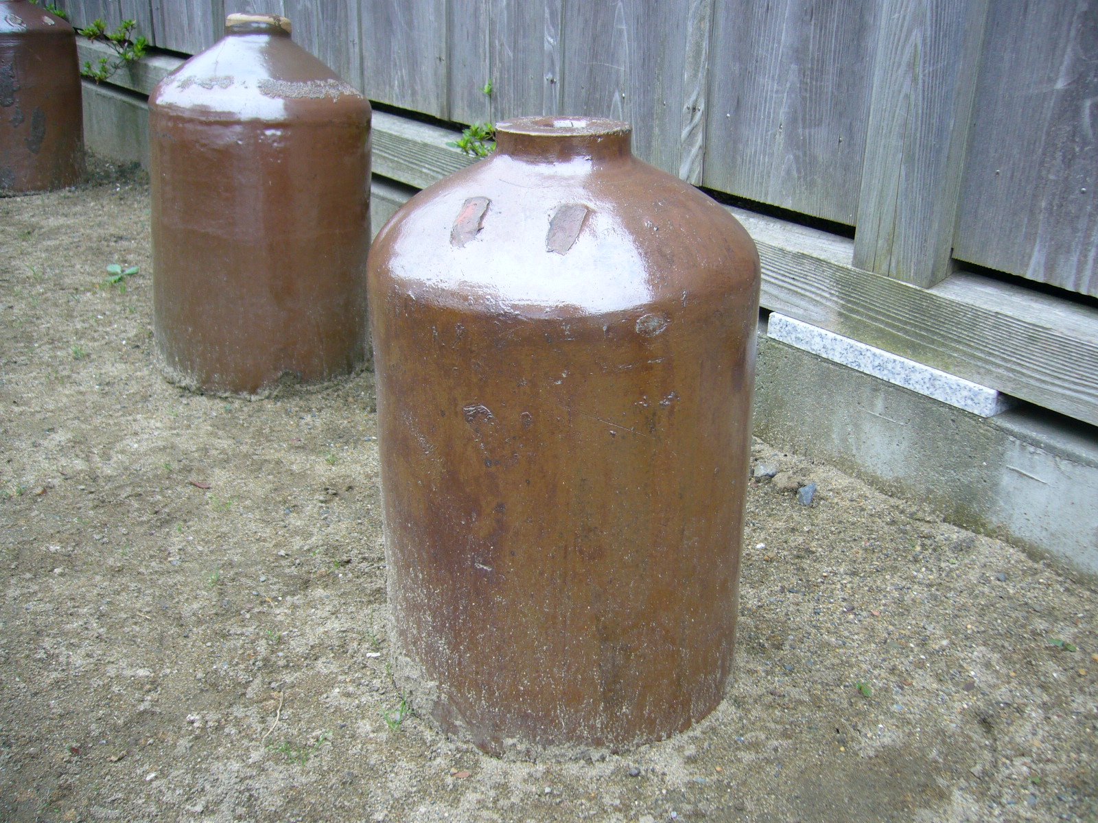 Two old glazed ceramic soy sauce jugs standing against a weathered timber wall