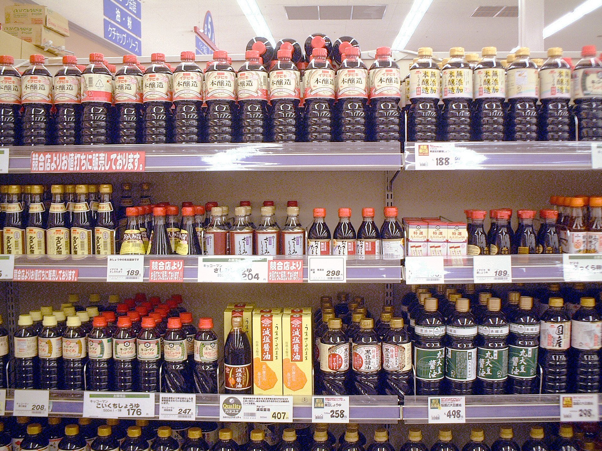 A Japanese supermarket soy sauce aisle — three shelves deep in bottles of every size and grade