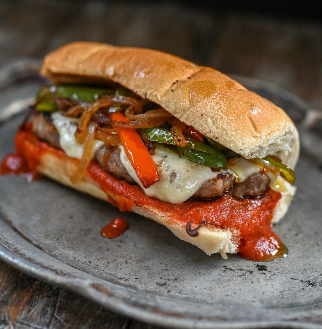 A cudighi sandwich on a bun, sausage patty under melted mozzarella and red sauce with onions