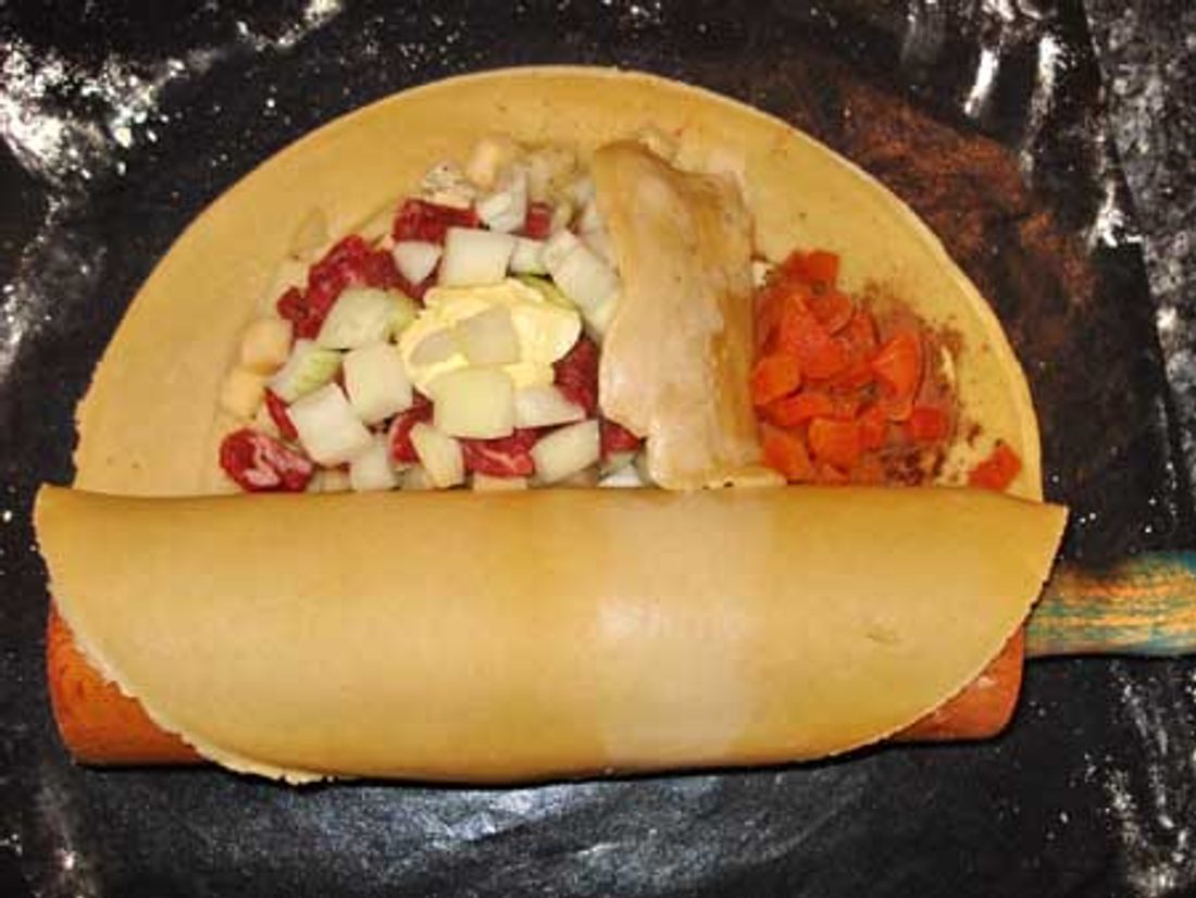 A hand holding a golden, crimped pasty with a bite taken out, showing the meat and vegetable filling