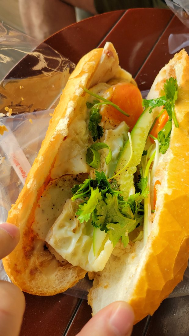 A bánh mì opened up — the split baguette, pâté, egg, coriander, chilli and pickled vegetable all visible at once