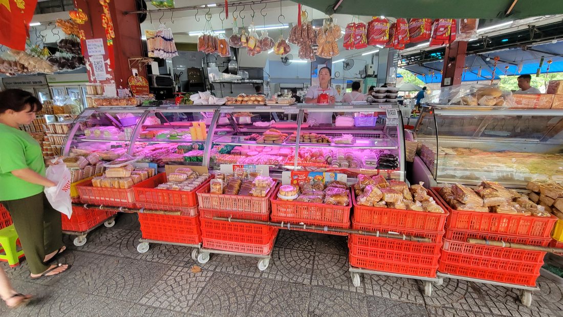 A deli case under pink light on the pavement, with red plastic crates on wheeled trolleys stacked below it — the day's bread and pastry, out on the street, at half past three in the afternoon