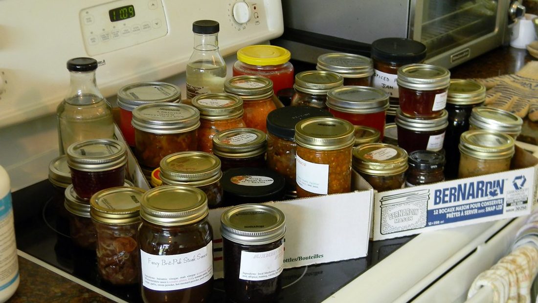 A dark, glossy homemade Worcestershire sauce being poured from a jar next to whole spices, tamarind, and anchovies