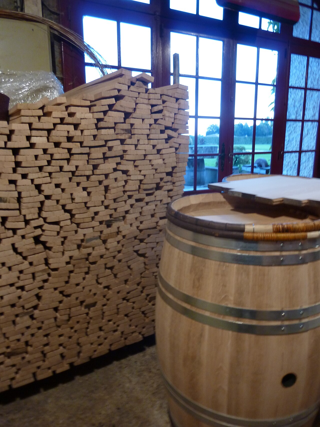 Fresh oak staves stacked at a cooperage next to a finished barrel — the flavor source we're borrowing from