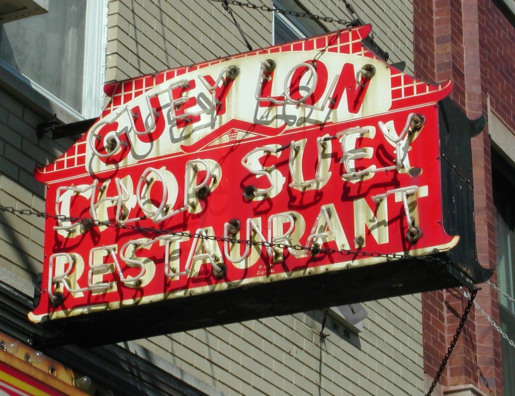 A red neon sign reading Guey Lon Chop Suey Restaurant on a building front